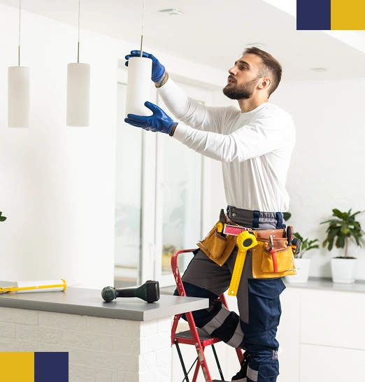 Een man in een bouwpakket hangt een hanglamp op in een pas gerenoveerde keuken.